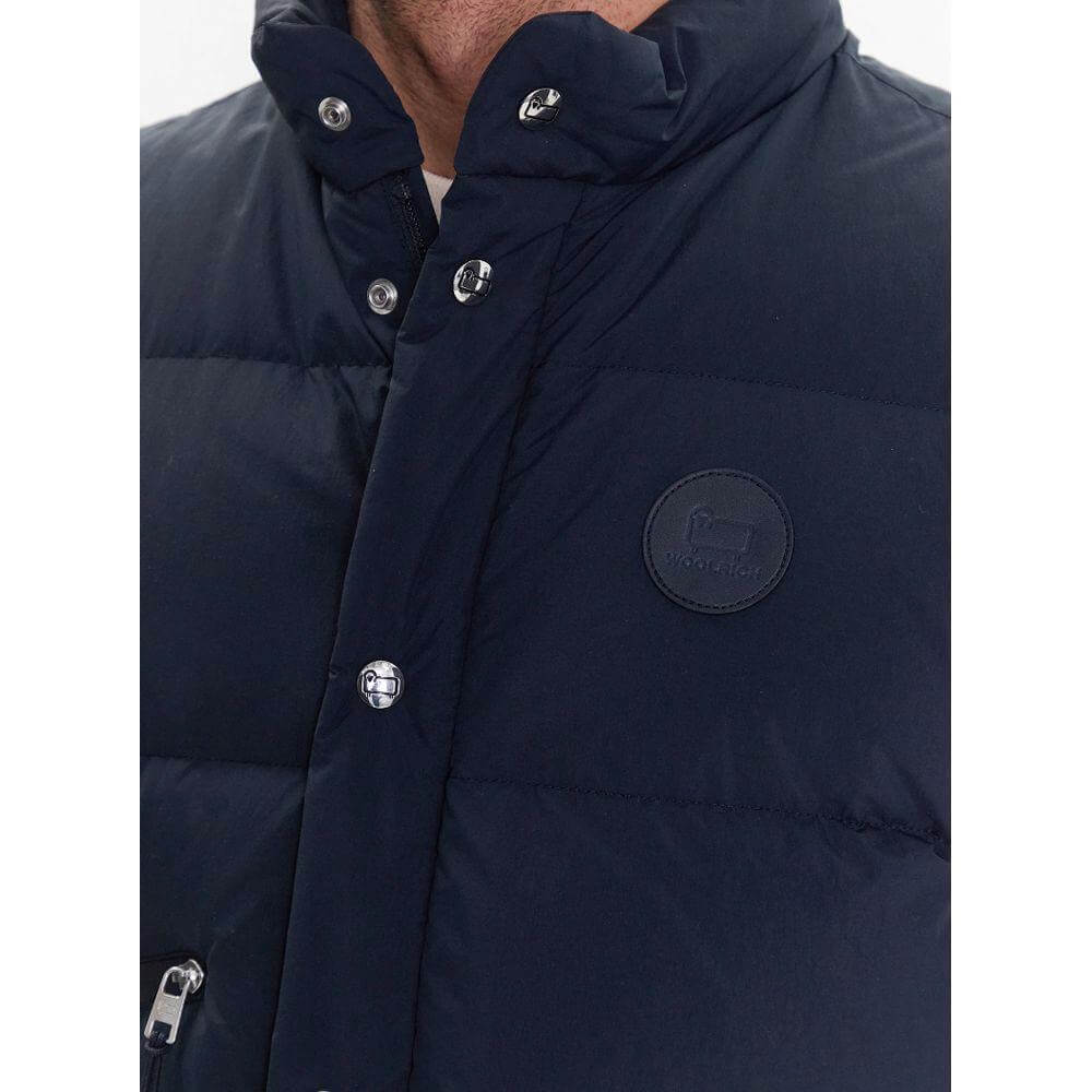 Close-up of Woolrich blue polyester vest with button and zip fastening, featuring goose down padding and logo patch.