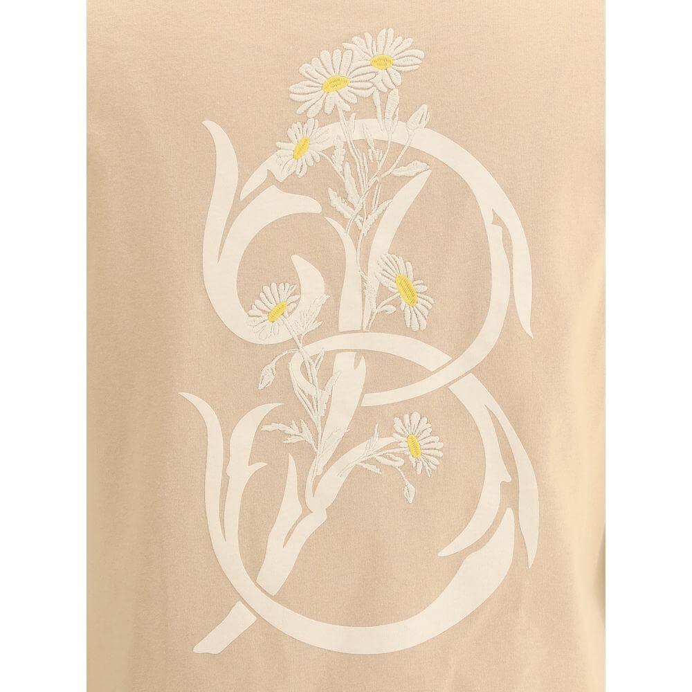 Burberry floral logo T-shirt featuring embroidered daisies and contrasting initial logo on soft cotton fabric with beige background.